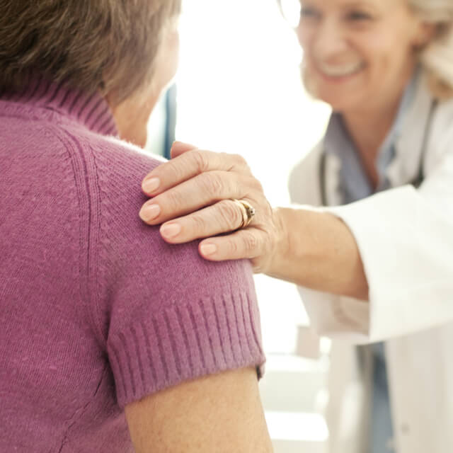 Una médica apoya la mano en el hombro de una paciente