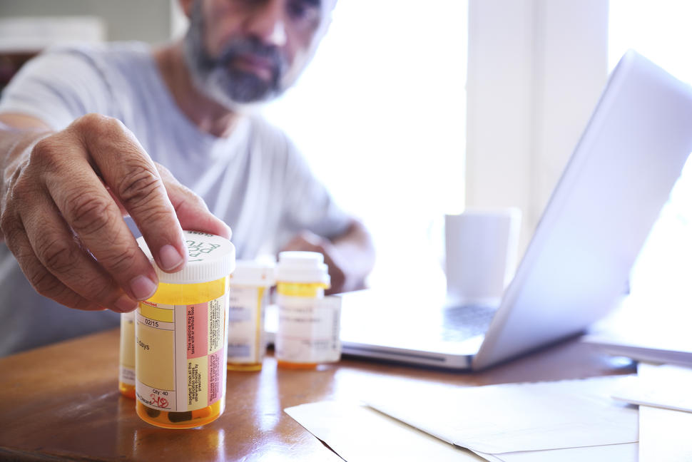 Foto en primer plano de un hombre alcanzando frascos de medicamentos recetados que están sobre una mesa